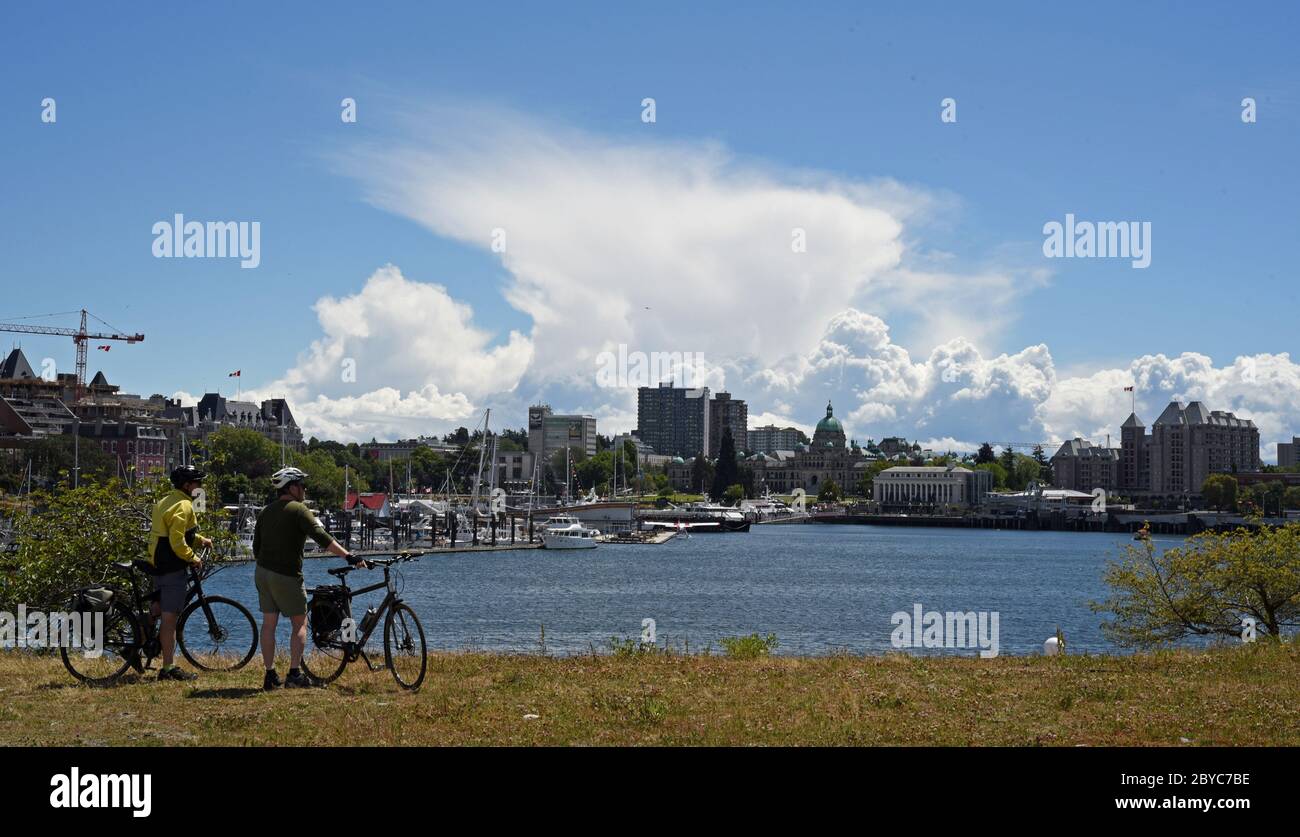 A pair of cyclists take in the view across the Inner Harbour in downtown Victoria, British Columbia, Canada on Vancouver Island looking towards the do Stock Photo