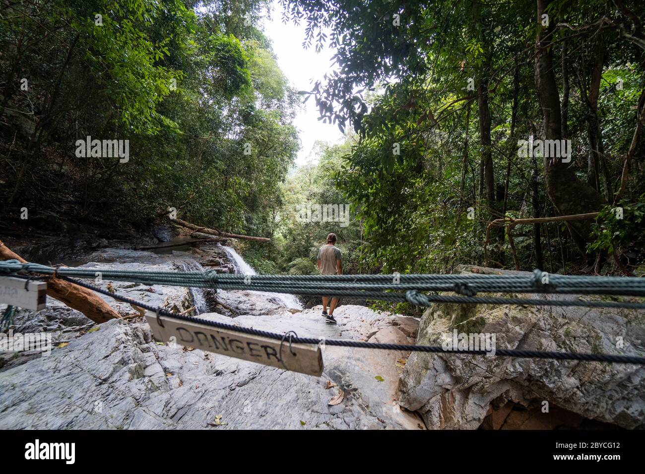 Man stands on rock on a top of waterfall with a danger sign which warns of  danger. Danger activity Stock Photo - Alamy