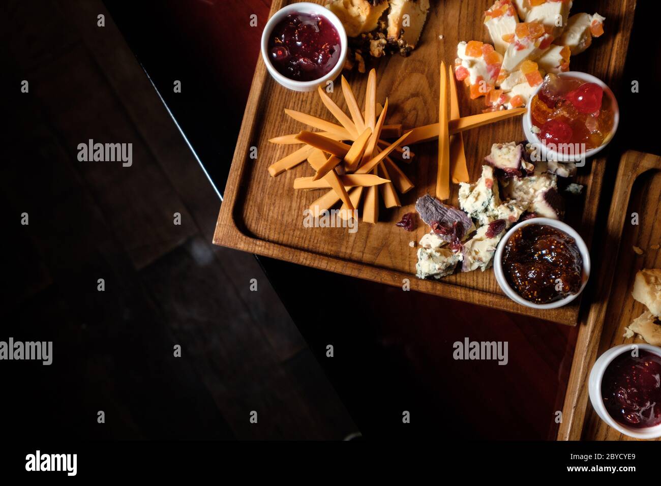 a top view of a wooden plate with various cheeses and jam, cut into small pieces on the table background, Flat lay Stock Photo