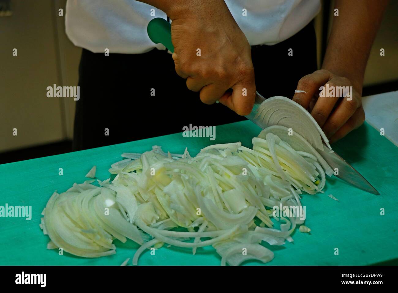 a chef slicing white onion on a green choping board Stock Photo