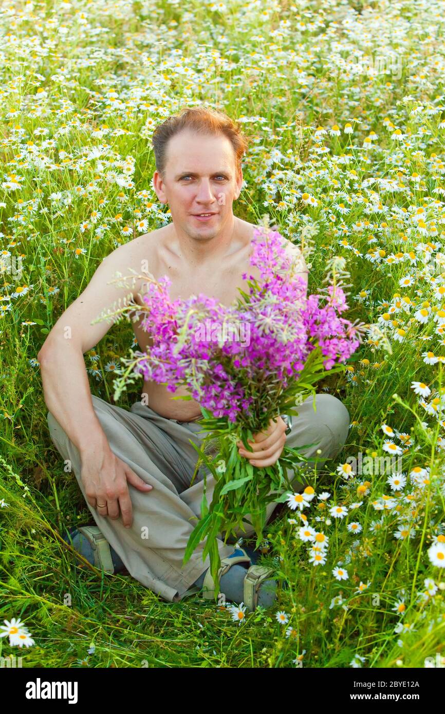 The man in the field of camomiles gives a bouquet Stock Photo