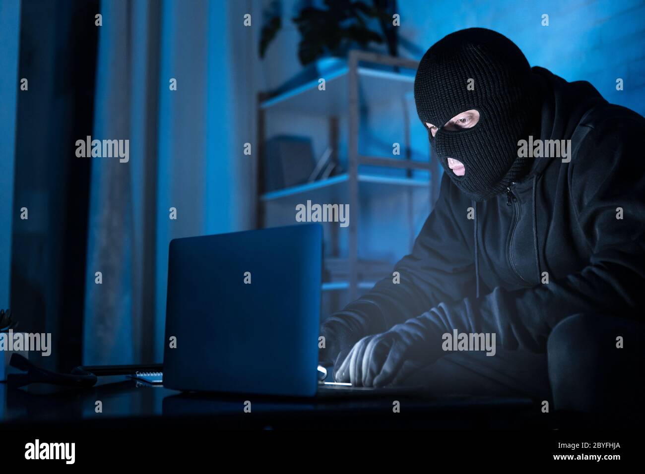 Masked hacker downloading private information using pc Stock Photo