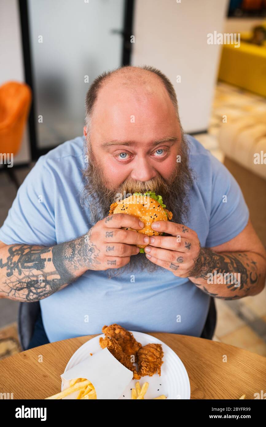 Bald man sitting at the table and eating a burger Stock Photo