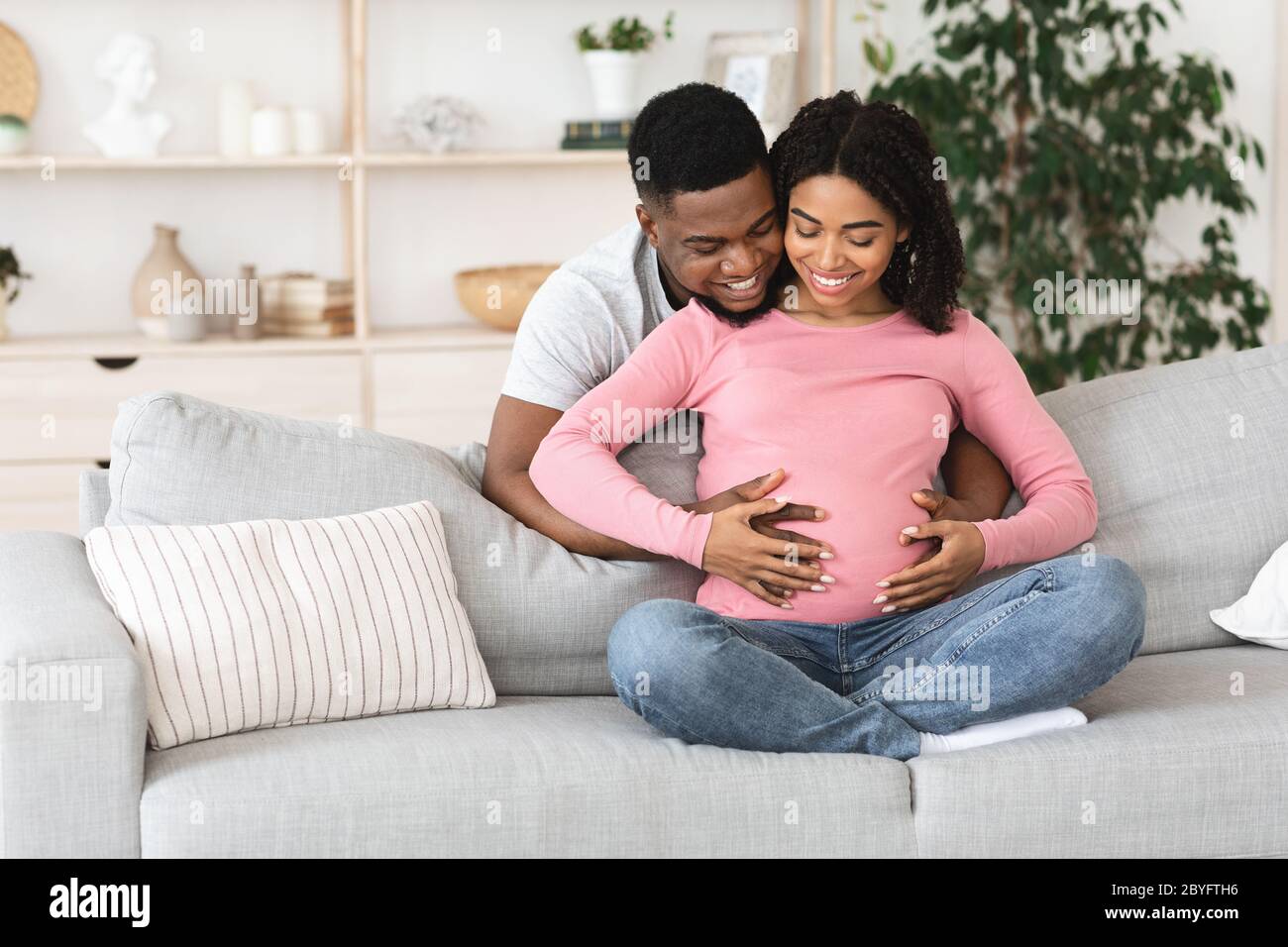 Happy young pregnant african couple cuddling at home Stock Photo - Alamy