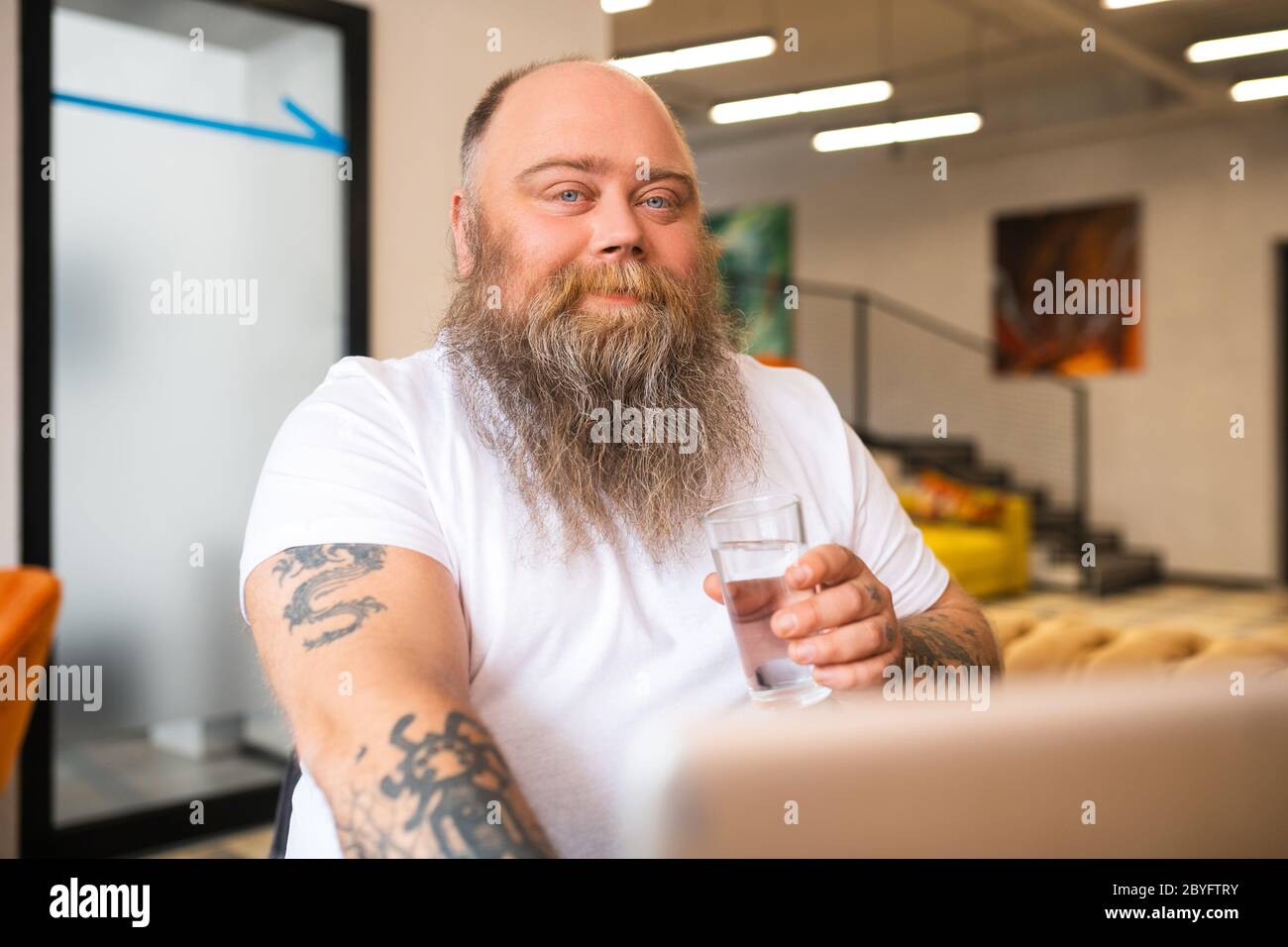 Bald bearded man in white tshirt holding a glass of water Stock Photo