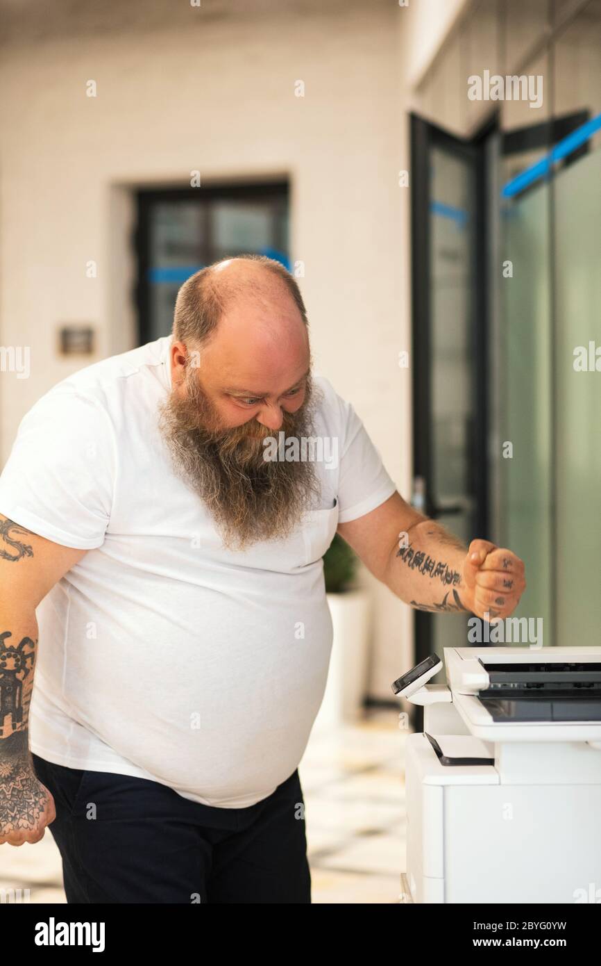 Bald bearded plus size man making copy on xerox and feeling angry Stock Photo