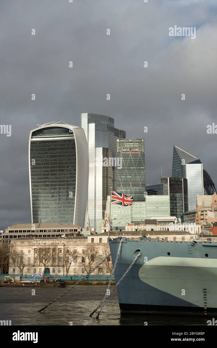 City of London glass buildings financial district skyline and bow of HMS Belfast as seen from South Bank in beautiful sunny weather with cloudy sky. Stock Photo