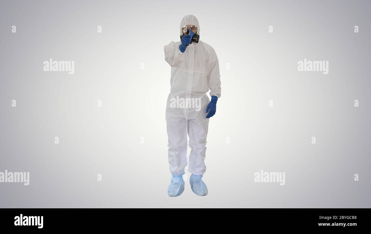 Doctor in protective biohazard suit points laser thermometer to check your temperature at a covid19 checkpoint on gradient background. Stock Photo