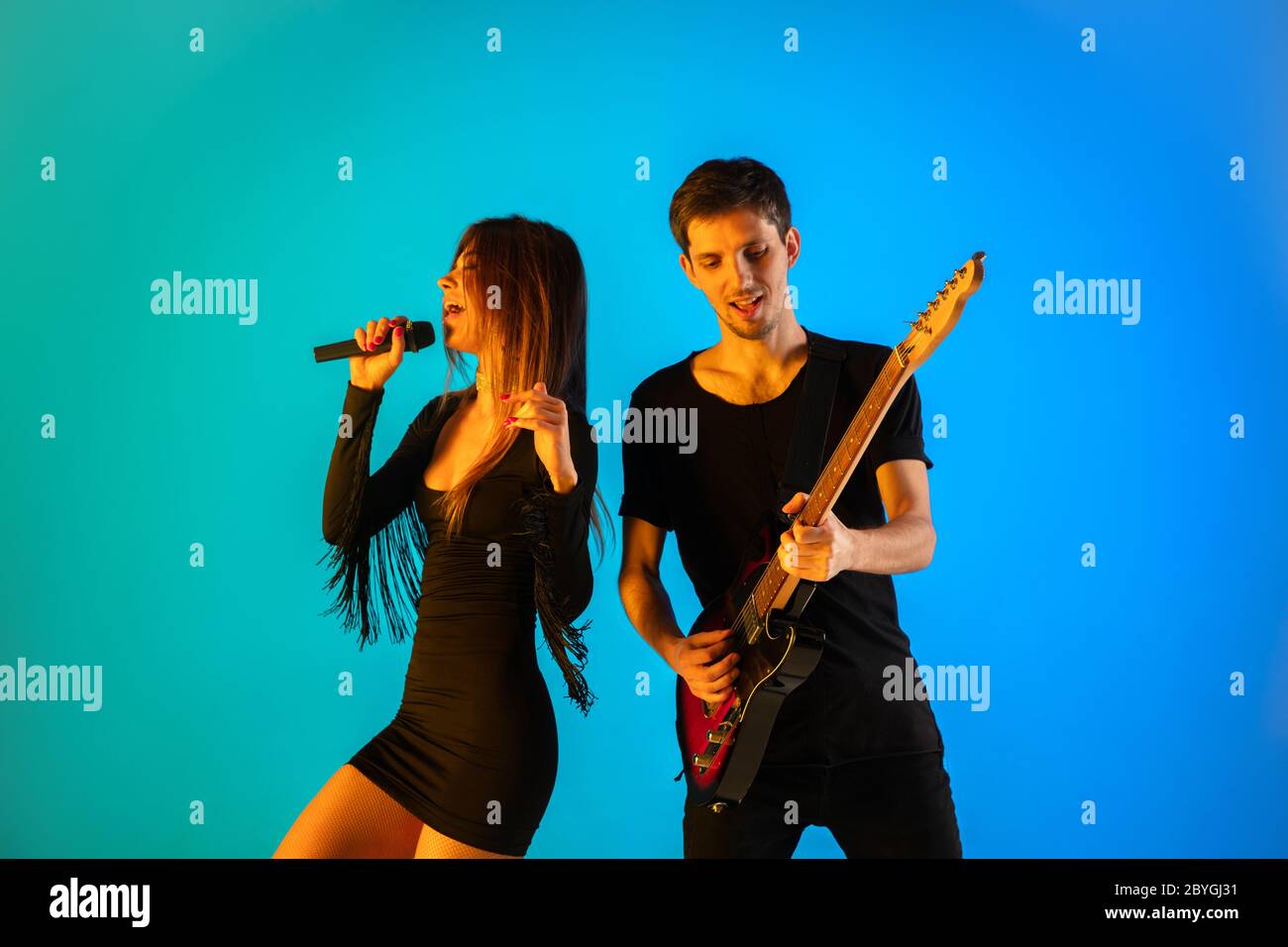 Caucasian musicians, singer and guitarist, isolated on blue studio background in neon light. Inspired improvising, performing. Concept of human emotions, facial expression, ad, music, art, festival. Stock Photo