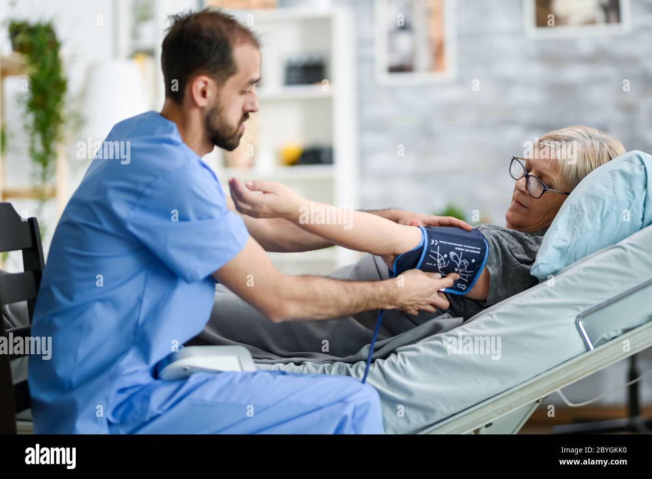 Young doctor in nursing home checking old woman blood pressure using digital device. Stock Photo