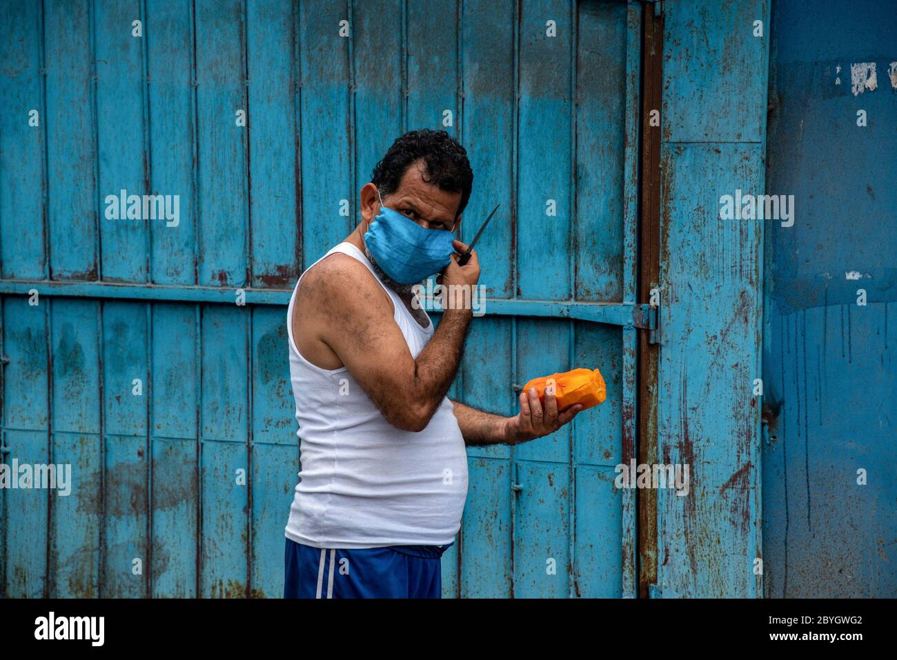 San Pedro Sula, Honduras. 23rd May, 2020. A man wearing a face mask as a preventive measure eats a pawpaw during the lockdown.Honduras instated a ''smart re-opening'' that allowed all commercial business to open, but demanded all employees and clients to wear masks. Credit: Seth Sidney Berry/SOPA Images/ZUMA Wire/Alamy Live News Stock Photo