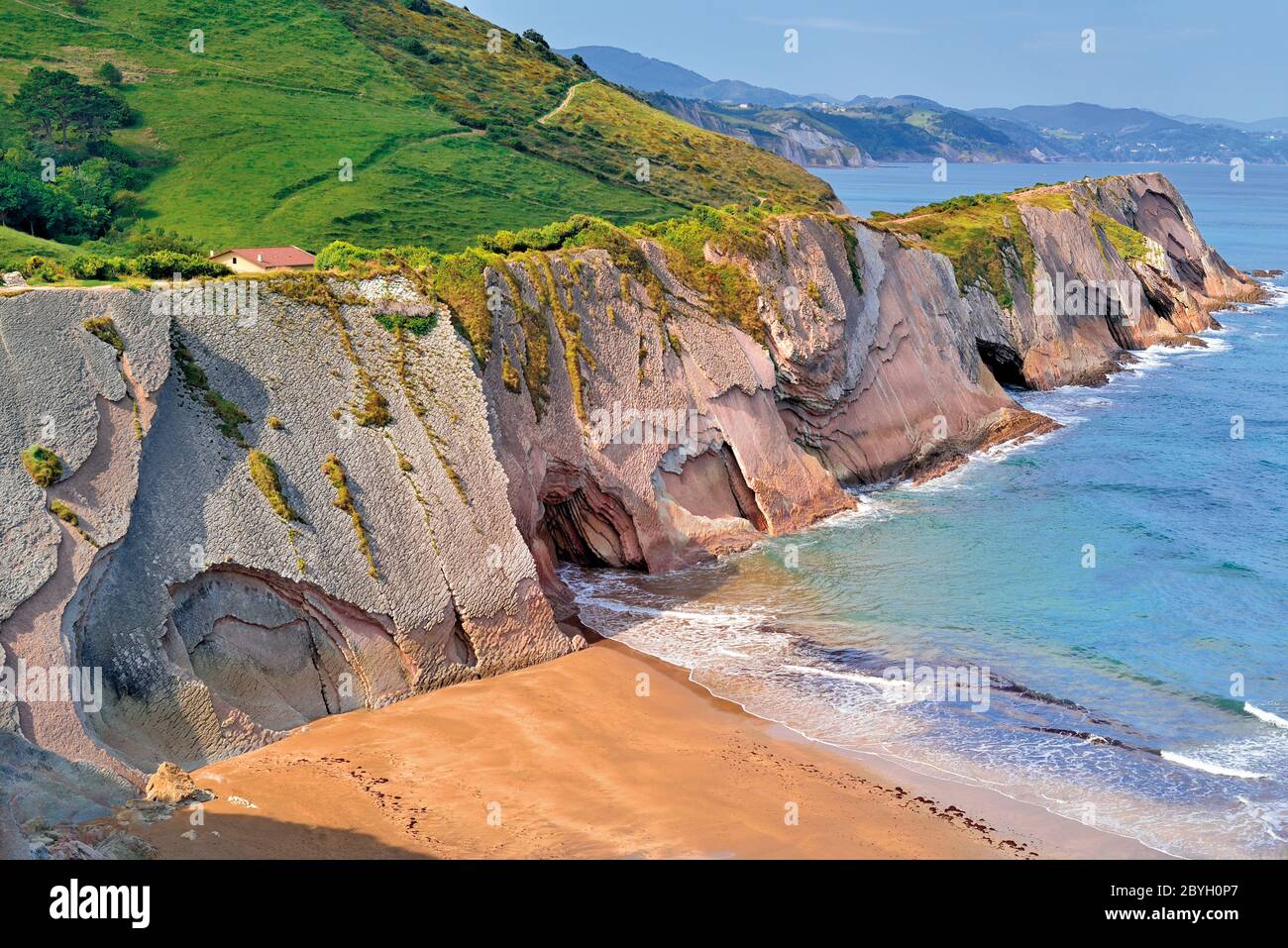 Great view of high rocky cliffs with green top, small chapel and sand beach at open ocean Stock Photo