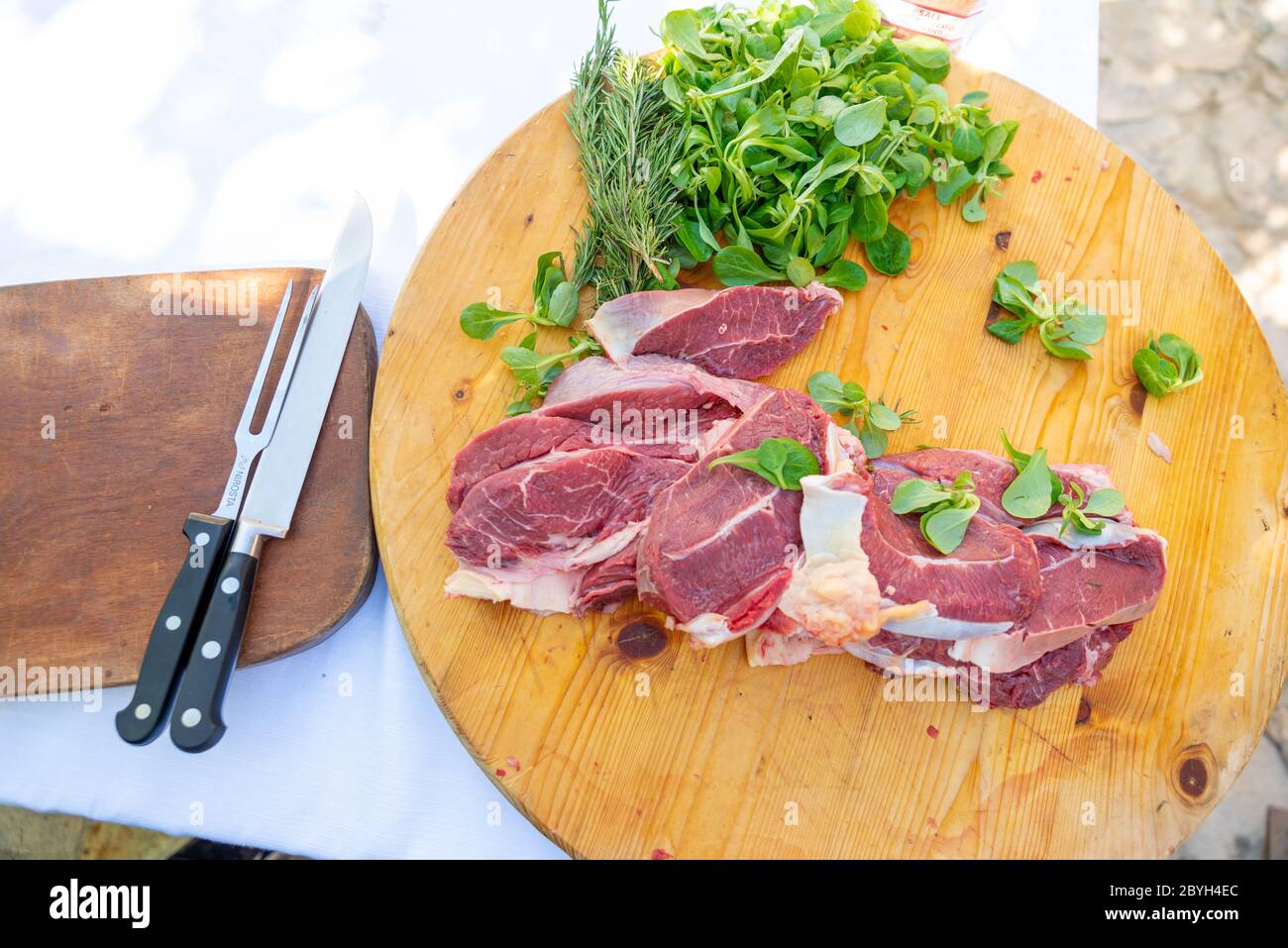 https://c8.alamy.com/comp/2BYH4EC/italy-beef-steaks-on-a-cutting-board-waiting-to-be-placed-on-the-barbeque-grill-steaks-with-salad-and-steak-knives-2BYH4EC.jpg