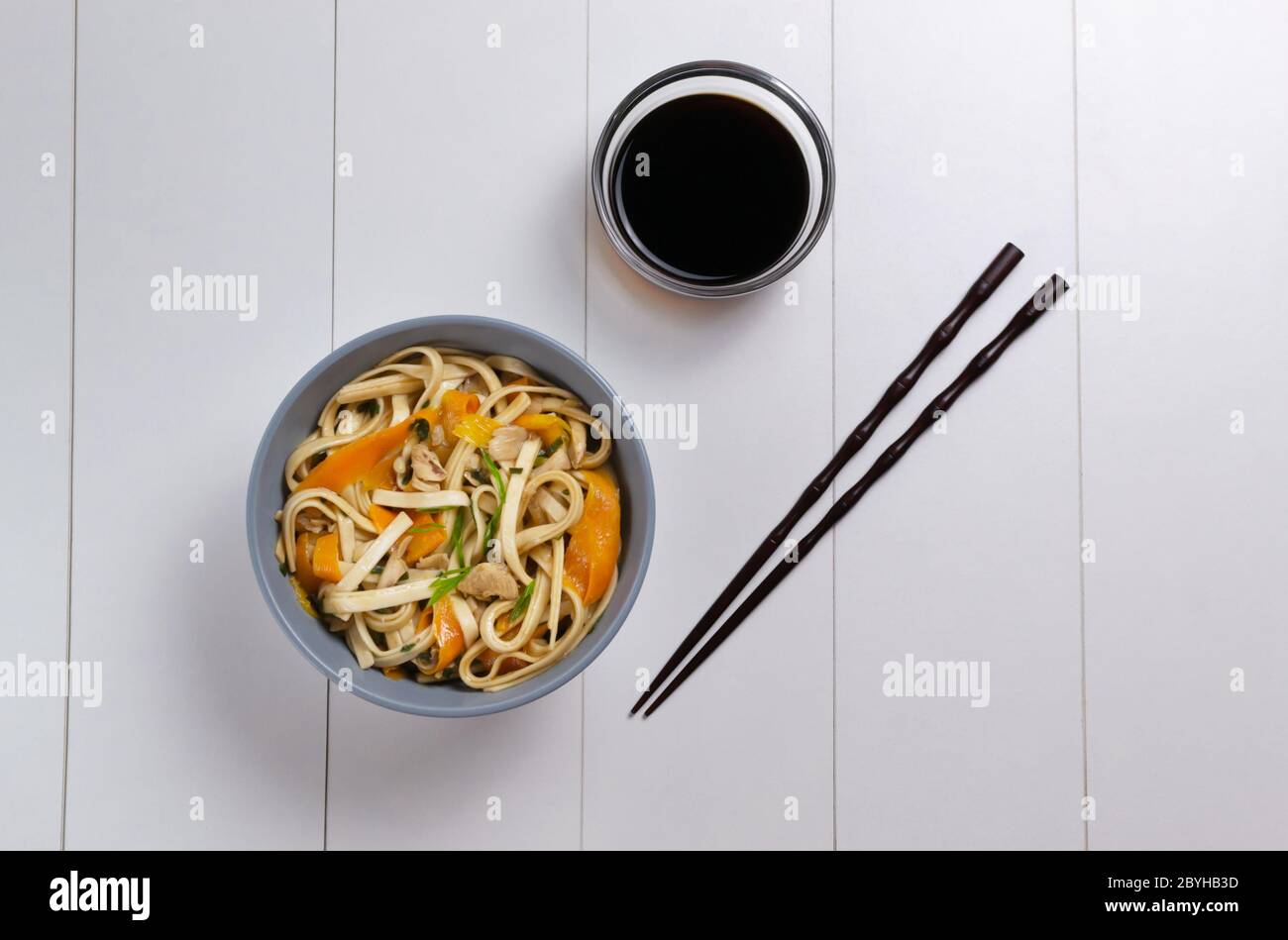 Udon noodles with chicken, soy sauce and bamboo sticks on a white plate. Top view. Japanese cuisine. Stock Photo