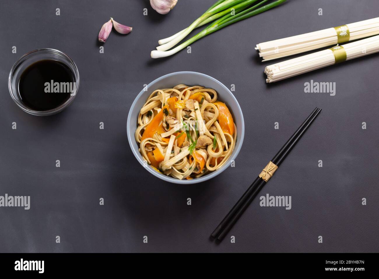 Udon noodles with chicken, soy sauce, bamboo sticks and fresh ingredients on a black background. Japanese cuisine. Stock Photo