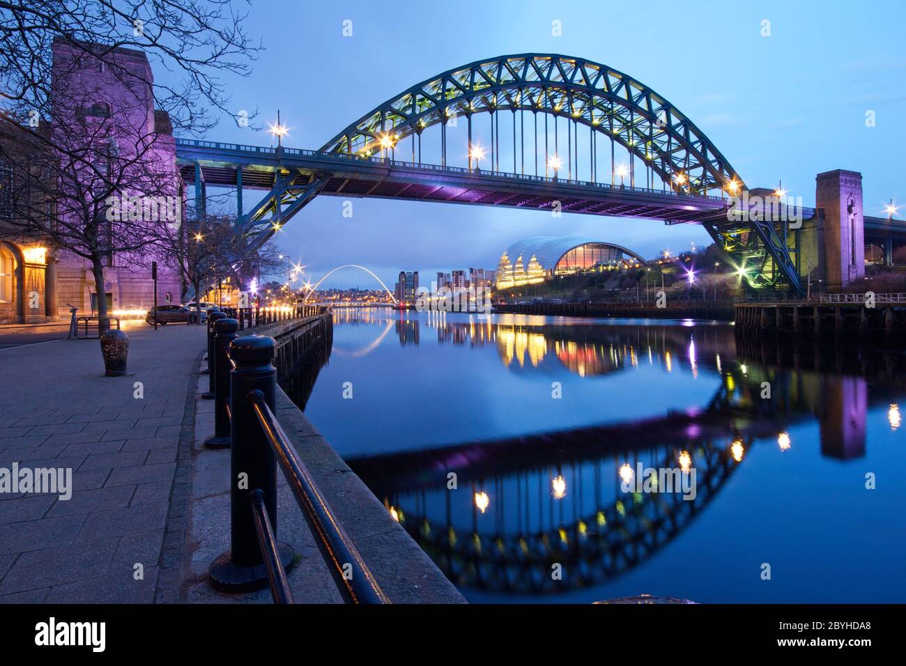 The green arch of the Tyne Bridge spanning the river joing Newcastle and Gateshead in Tyne and Wear with reflections in the still water and the Sage C Stock Photo