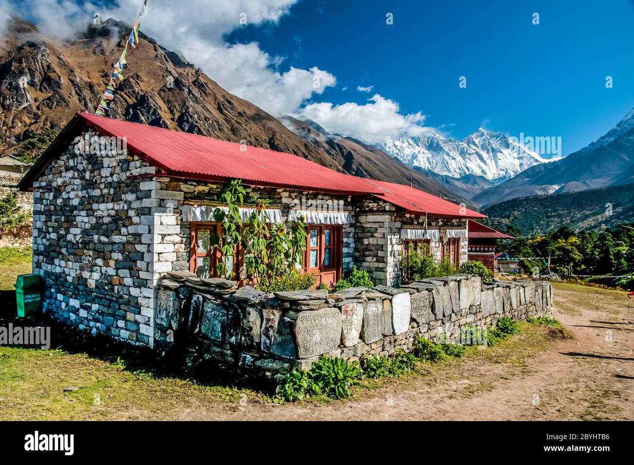 Nepal. Trek to Island Peak. Colourful scenes in and around the Thyangboche Buddhist Monastery with one of the resident monks Bungalow with Mani stone prayer wall and Mount Everest in the distant clouds Stock Photo