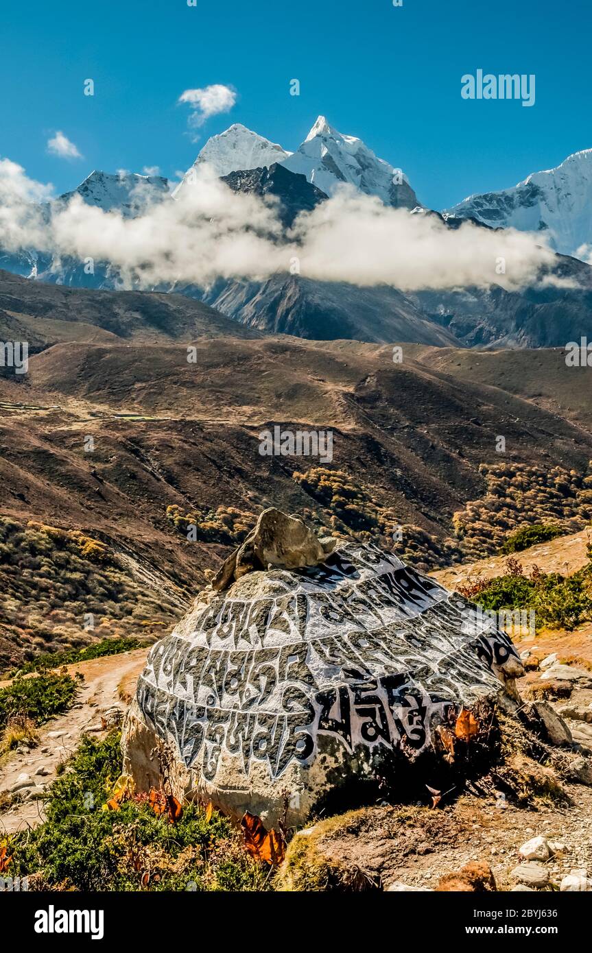 Nepal.Island Peak Trek. Buddhist mani stone prayer wall with the engraved Buddhist mantra of Om Mani Padmi Hum looking towards the peaks of Ama Dablam from above the Sherpa settlement of Dingboche Stock Photo