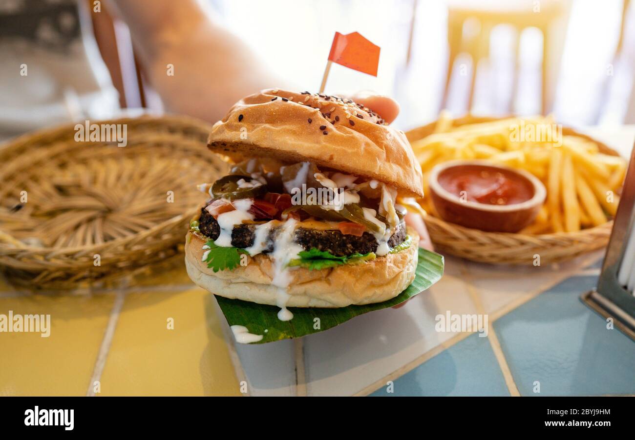 Freshly made of healthy vegan burger,  dish represented on wooden plate. Man's hands taking vegan burger from plate in vegan restaurant or cafe. Stock Photo