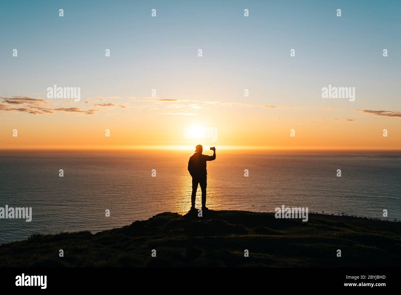 Silhouette of a young man watching sunset at the seaside and taking ...