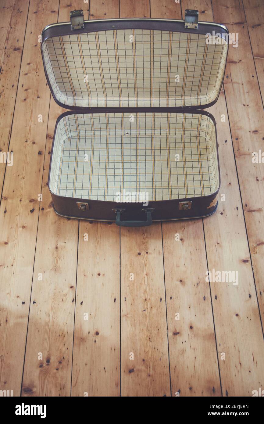 An open old vintage brown travel suitcase on a wooden floor Stock Photo