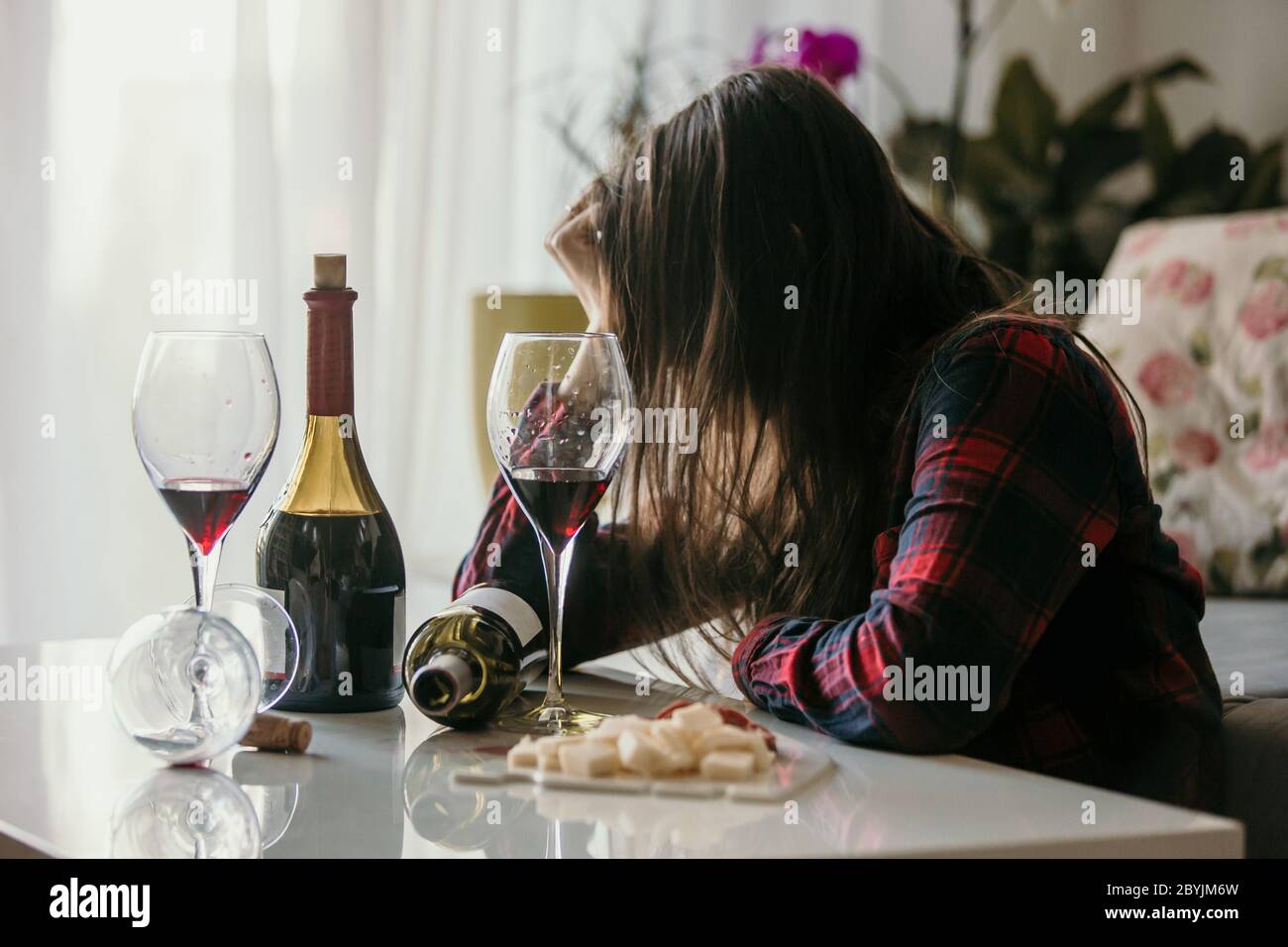 Sad tired woman, drinking wine at home, alone, sitting on the floor in living room, feeling