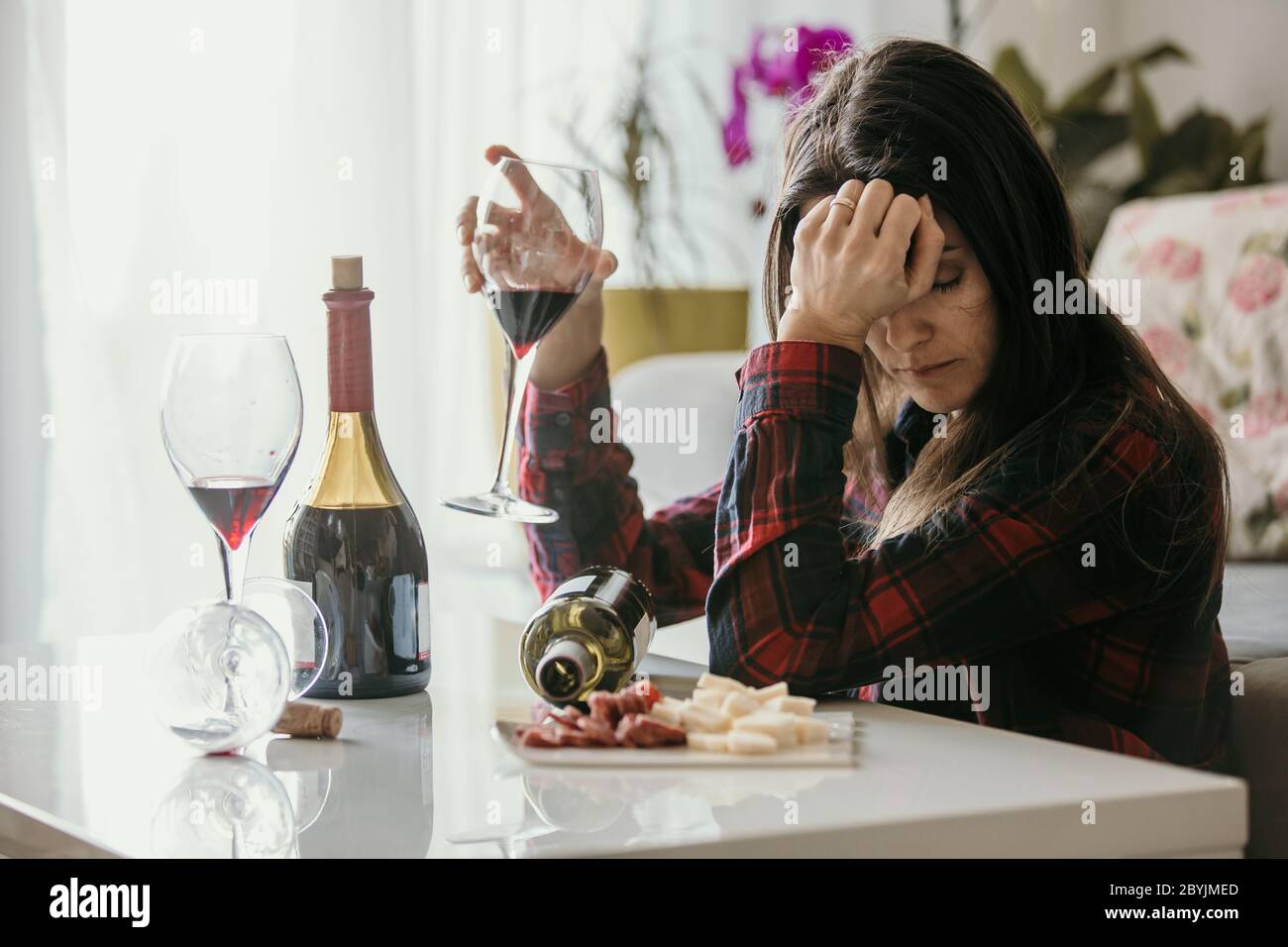 Sad tired woman, drinking wine at home, alone, sitting on the floor in