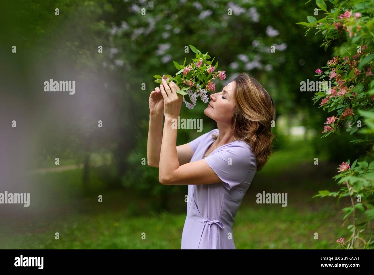 Woman in lilac dress sniffs bouquet of flowers with closed eyes and ...