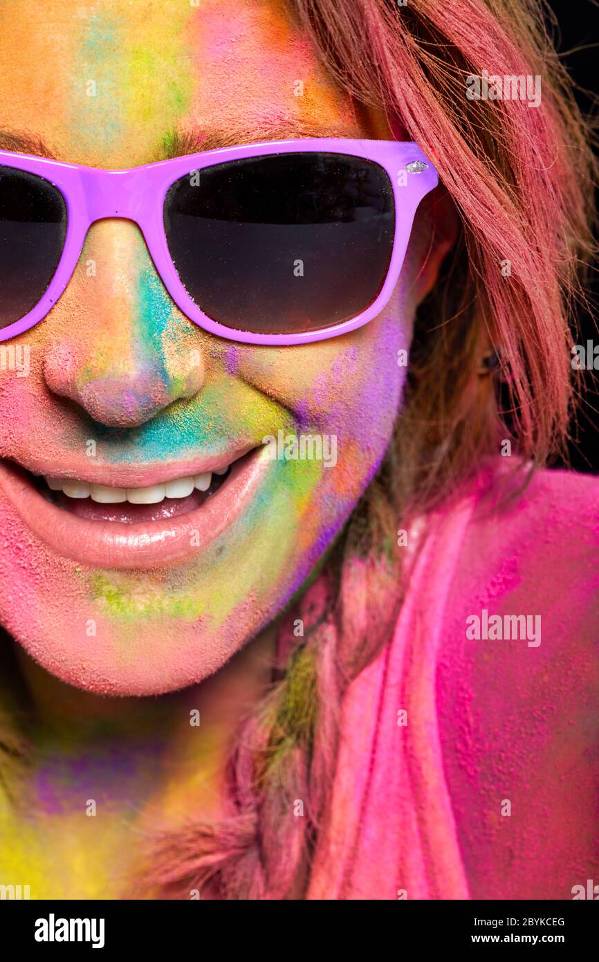 Beautiful young woman covered in rainbow colored Holi powder. Closeup cheerful model girl in colorful sunglasses and face covered with colorful powder Stock Photo