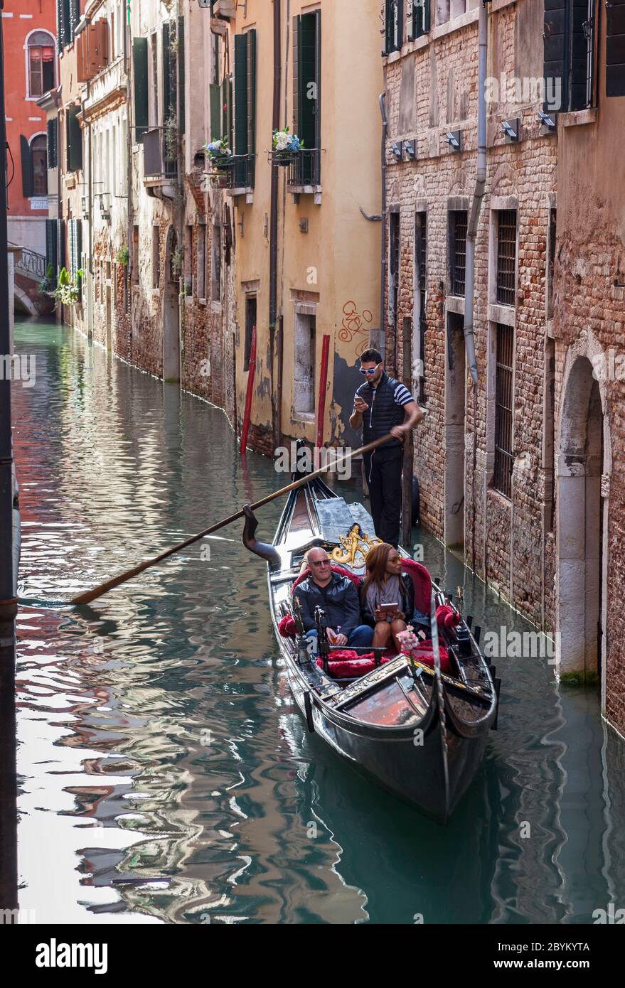 Couple on a gondola trip on the Rio de San Salvador canal in Venice, Italy while the gondolier is distracted using his mobile phone Stock Photo