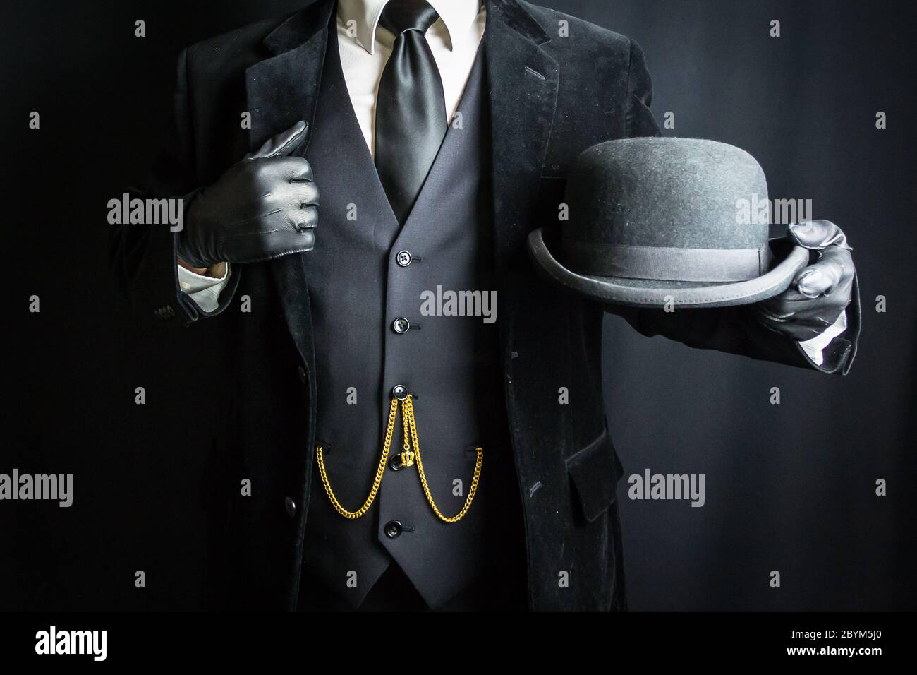 Portrait of Well Dressed Man in Dark Suit and Leather Gloves Holding Bowler Hat. Concept of Classic and Eccentric British Gentleman. Retro Fashion. Stock Photo