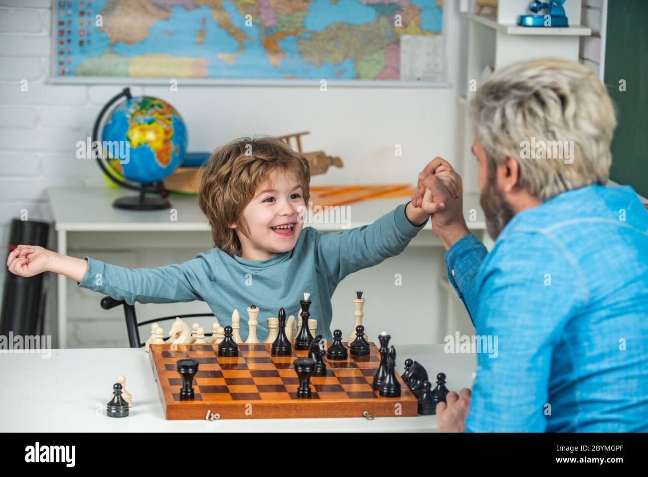 Young kid boy playing chess with father and having fun. Education and learning people concept - pupil and Teacher Stock Photo