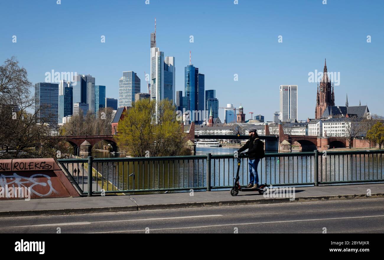 01.04.2020, Frankfurt am Main, Hesse, Germany - Man driving an electric scooter during the Corona crisis with a ban on contact, with the skyline of do Stock Photo
