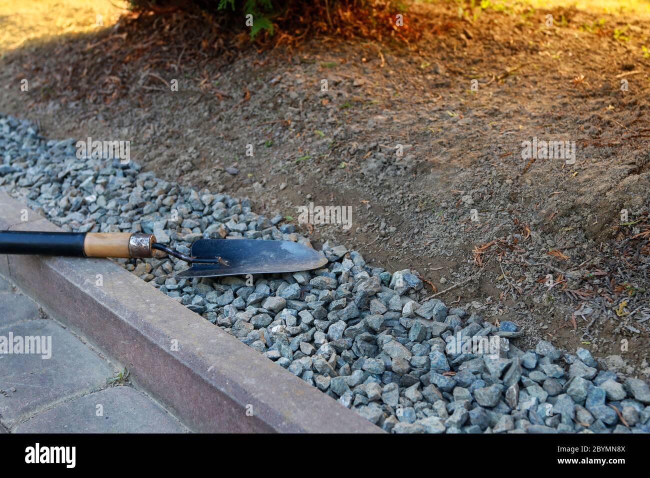Gardener at work: How to make a decoration from small pebbles next to a path in the garden. Stock Photo