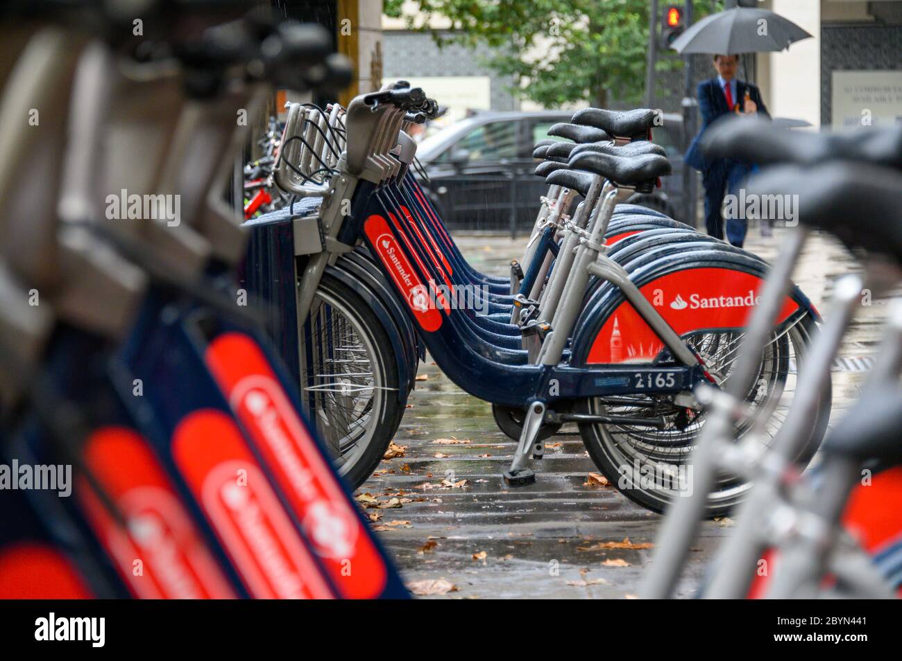 LONDON - SEPTEMBER 23, 2019: A line of 'Boris Bikes' for hire with a man walking past carrying an umbrella along The Strand on a rainy day Stock Photo