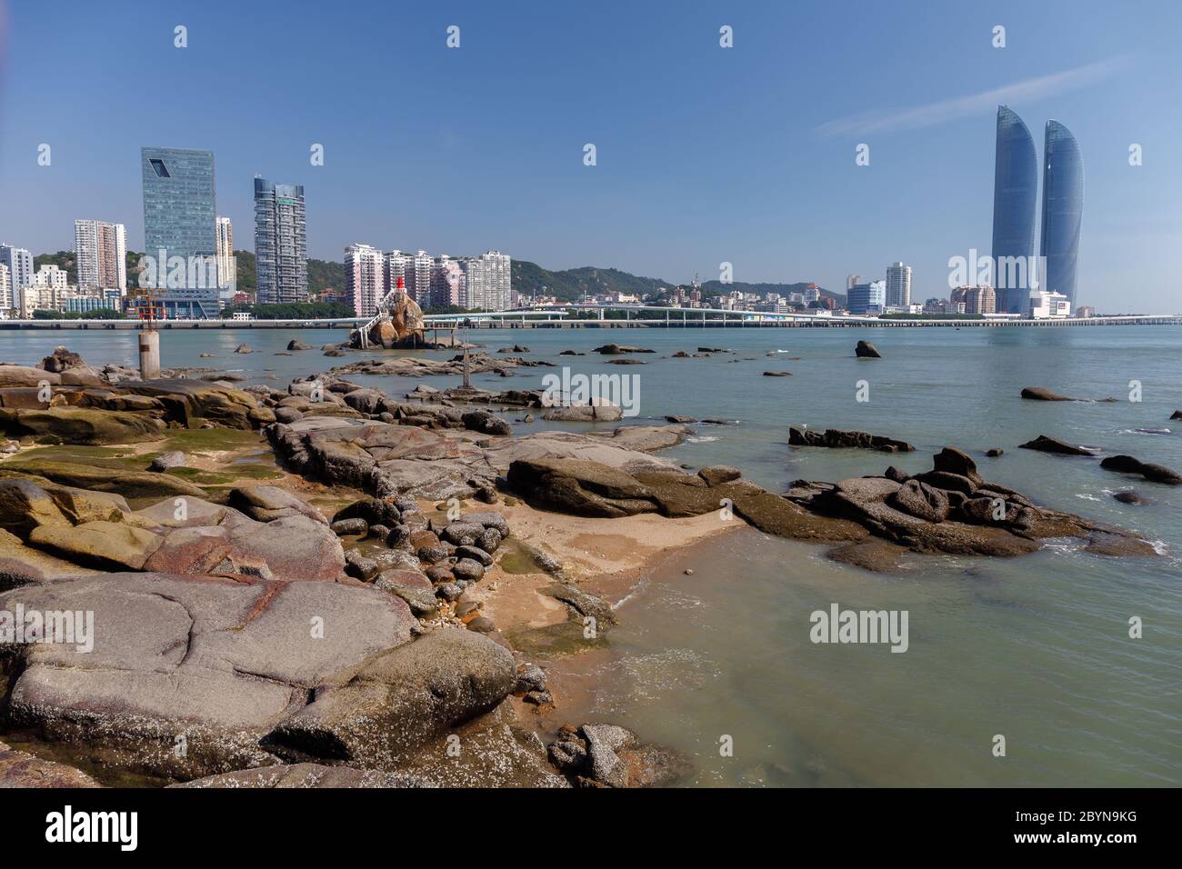 Skyline of Xiamen with Shimao Straits Towers. Rocky shore in the foreground. Stock Photo
