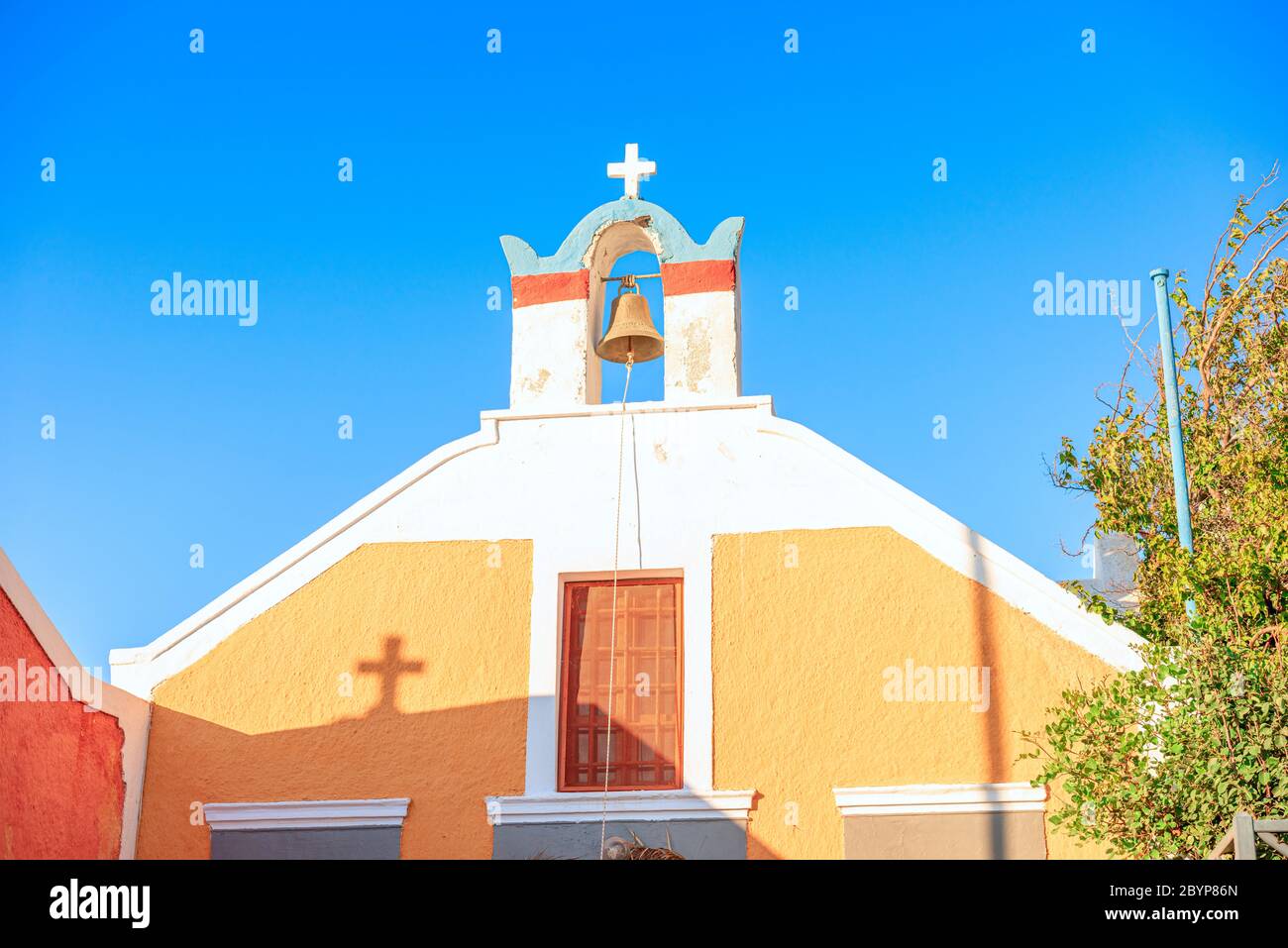 Colourful Greek church against a blue sky with a shadow of the cross falling on the building in Oia, Santorini, Greece Stock Photo