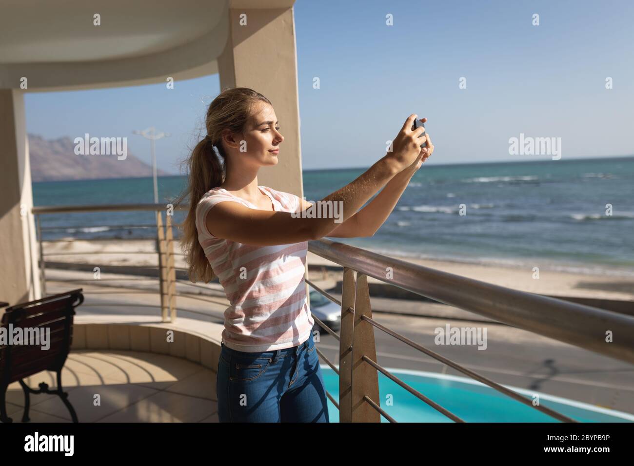 Caucasian woman standing on a balcony holding a smartphone and taking a selfie Stock Photo