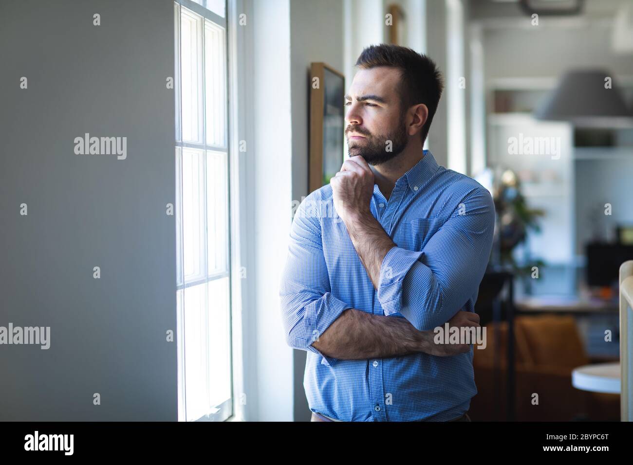 Caucasian man thinking next to a window in an office Stock Photo