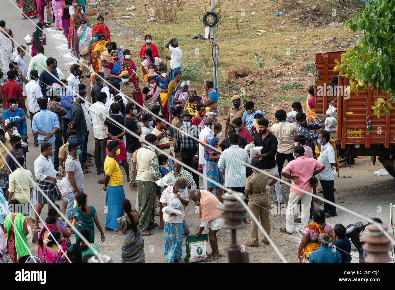 A group of people gather to receive free groceries and rice despite concerns about the spread of COVID-19. The crowd is watched by police, yet some pe Stock Photo