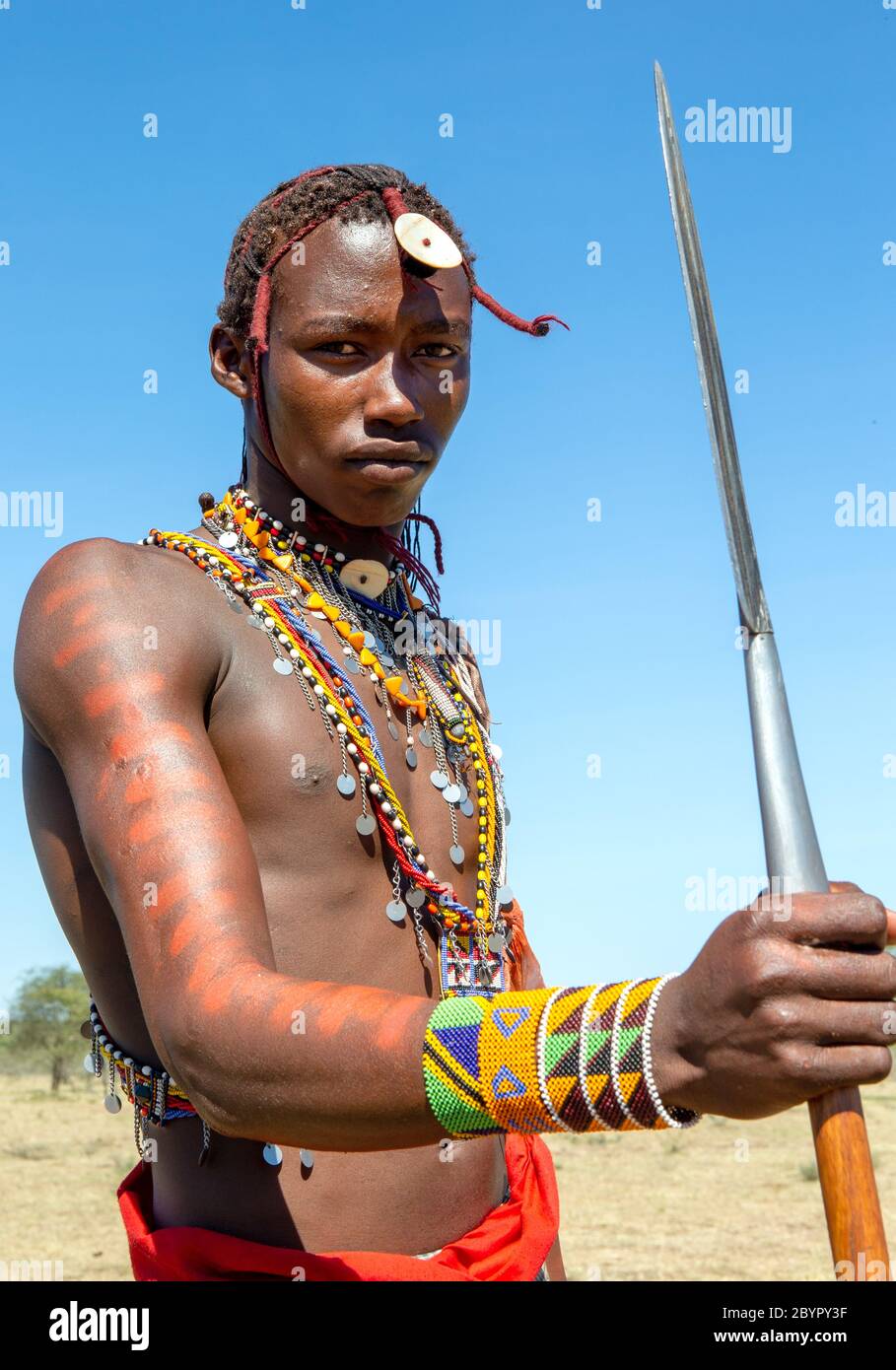 Portrait of a young Masai warrior in traditional clothing with a spear  against a blue sky. Tanzania, East Africa, August 12, 2018 Stock Photo -  Alamy, image size:909x1390