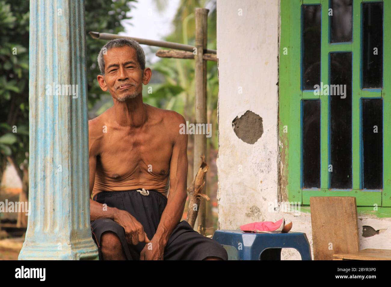 Probolinggo, Indonesia - June 14, 2013: Old Indonesian man on porch of his house in a village in Java. Walking in the countryside of an Indonesian vil Stock Photo