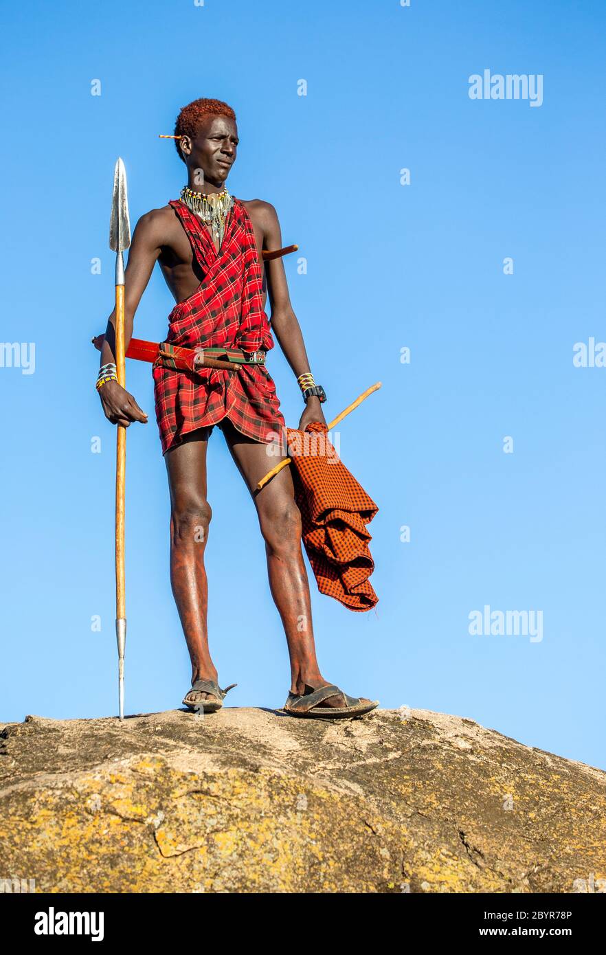 Young Masai warrior is standing on a big stone in traditional 