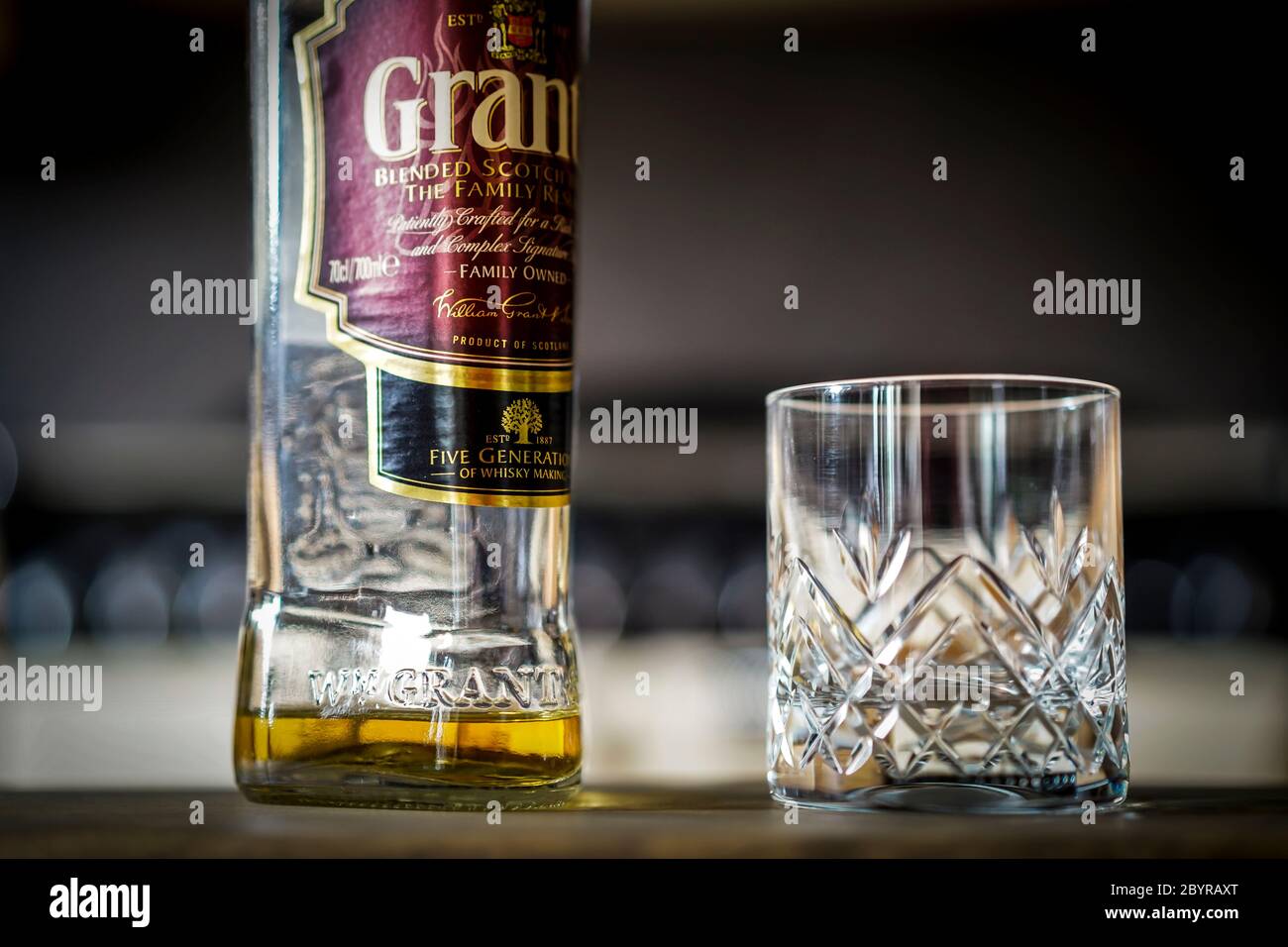 Grant's scotch whisky bottle and empty crystal whisky tumbler glass on kitchen table. Drinking alcohol at home in UK lockdown. Stock Photo