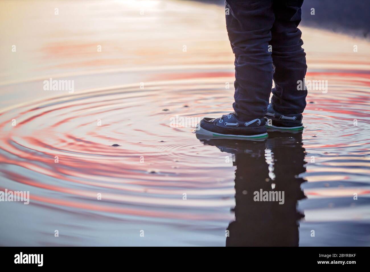 Sweet toddler child, cute boy with red raincoat, playing in puddle on