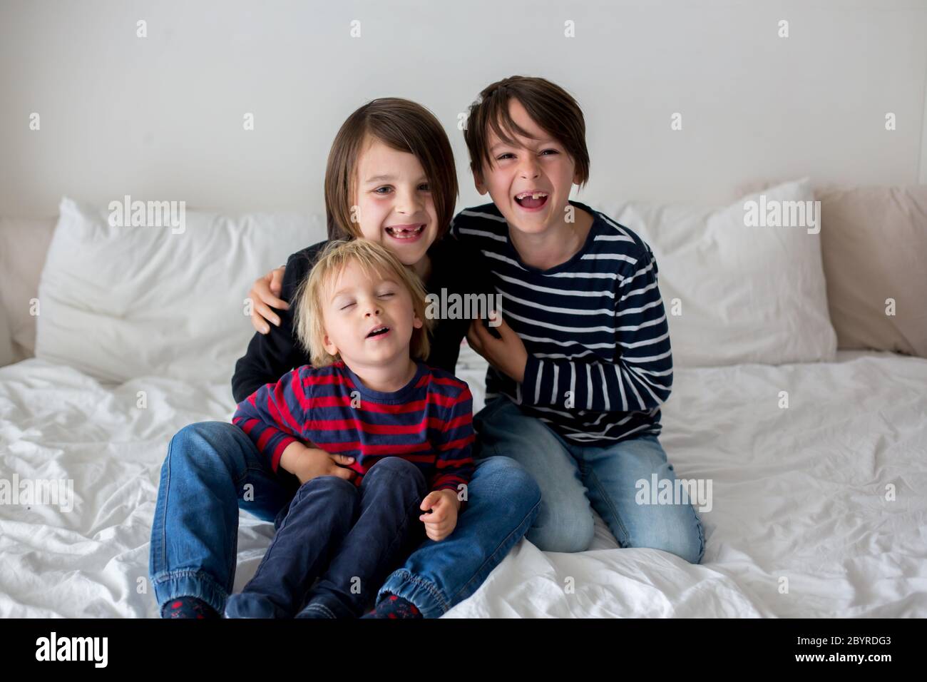 Three children, boy brothers, laughing in bed, gigling and tickling