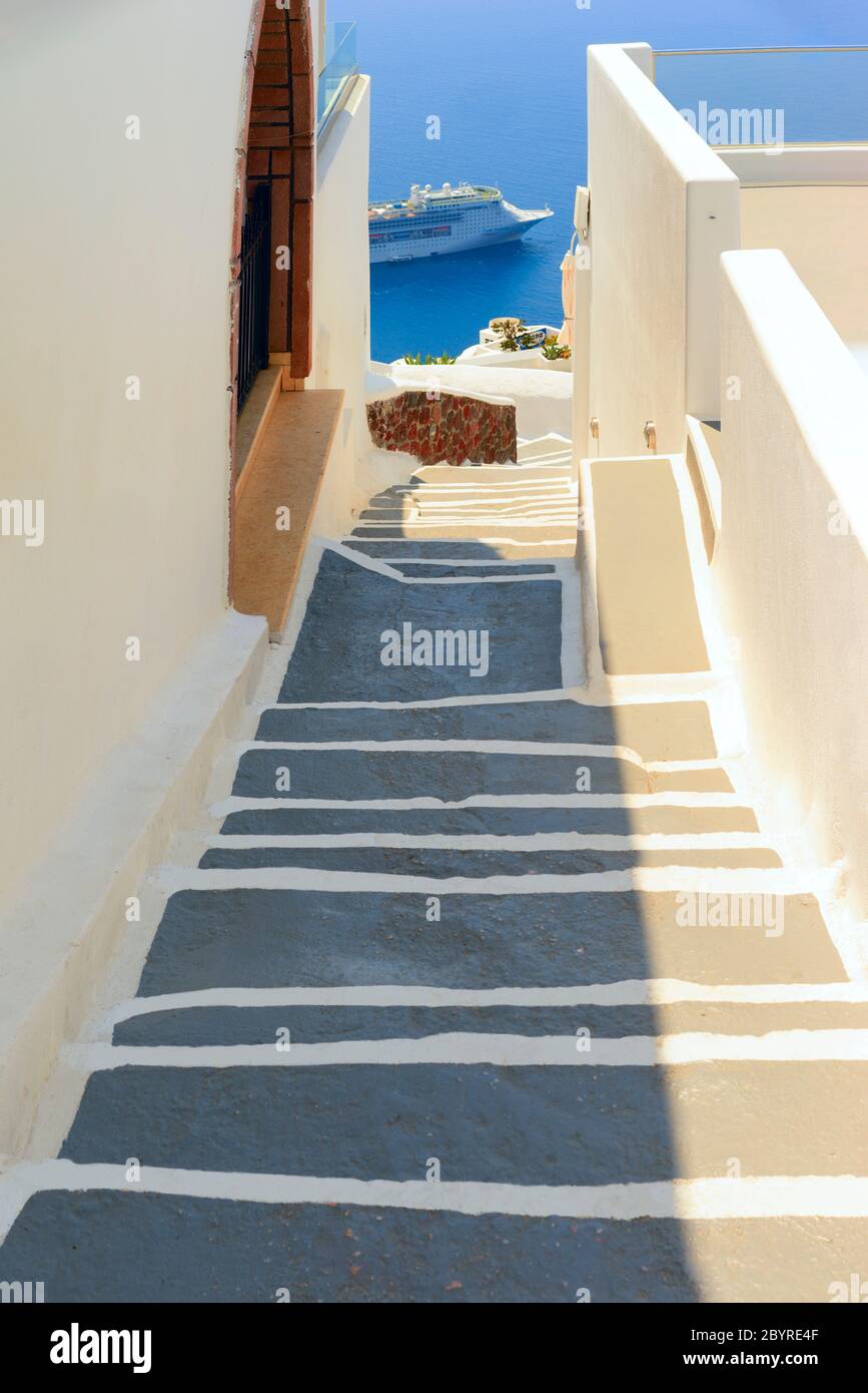Steps lead down the edge of the caldera through the white painted village on the Greek island of Santorini overlooking a cruise ship on the Aegean Sea Stock Photo