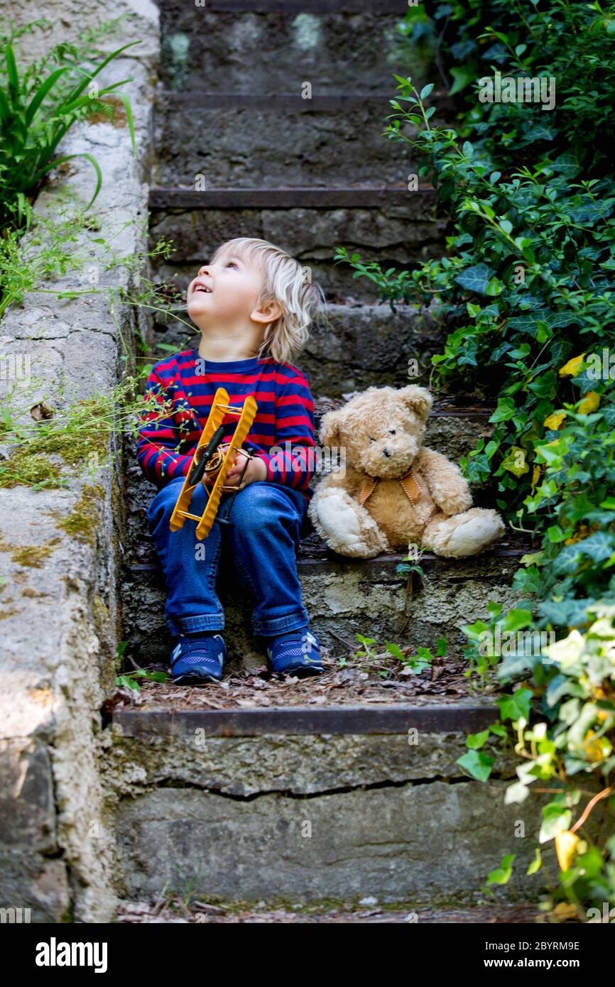 Cute little todller boy, sitting on stairs with teddy bear, playing ...