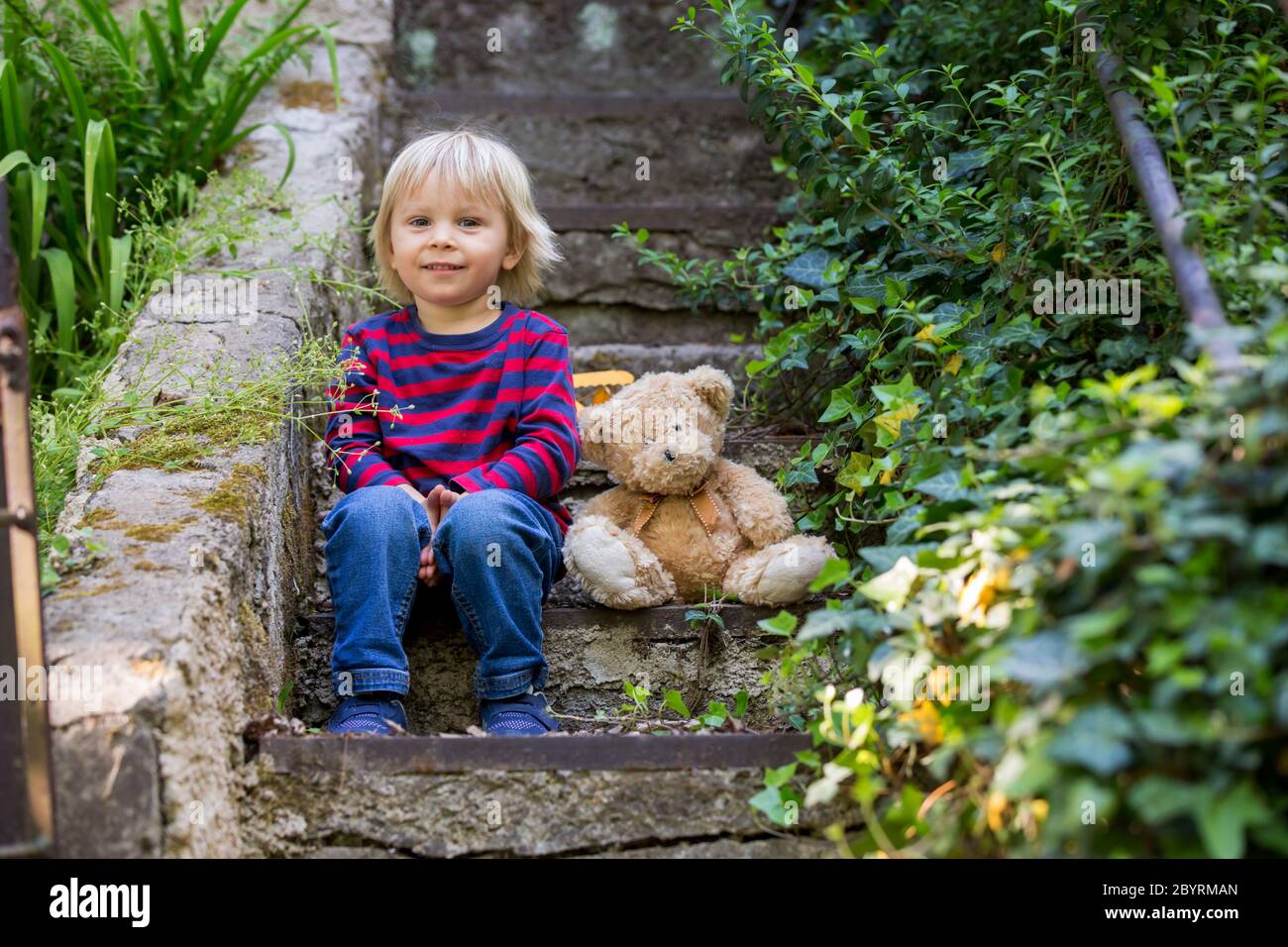 Cute little todller boy, sitting on stairs with teddy bear, playing ...
