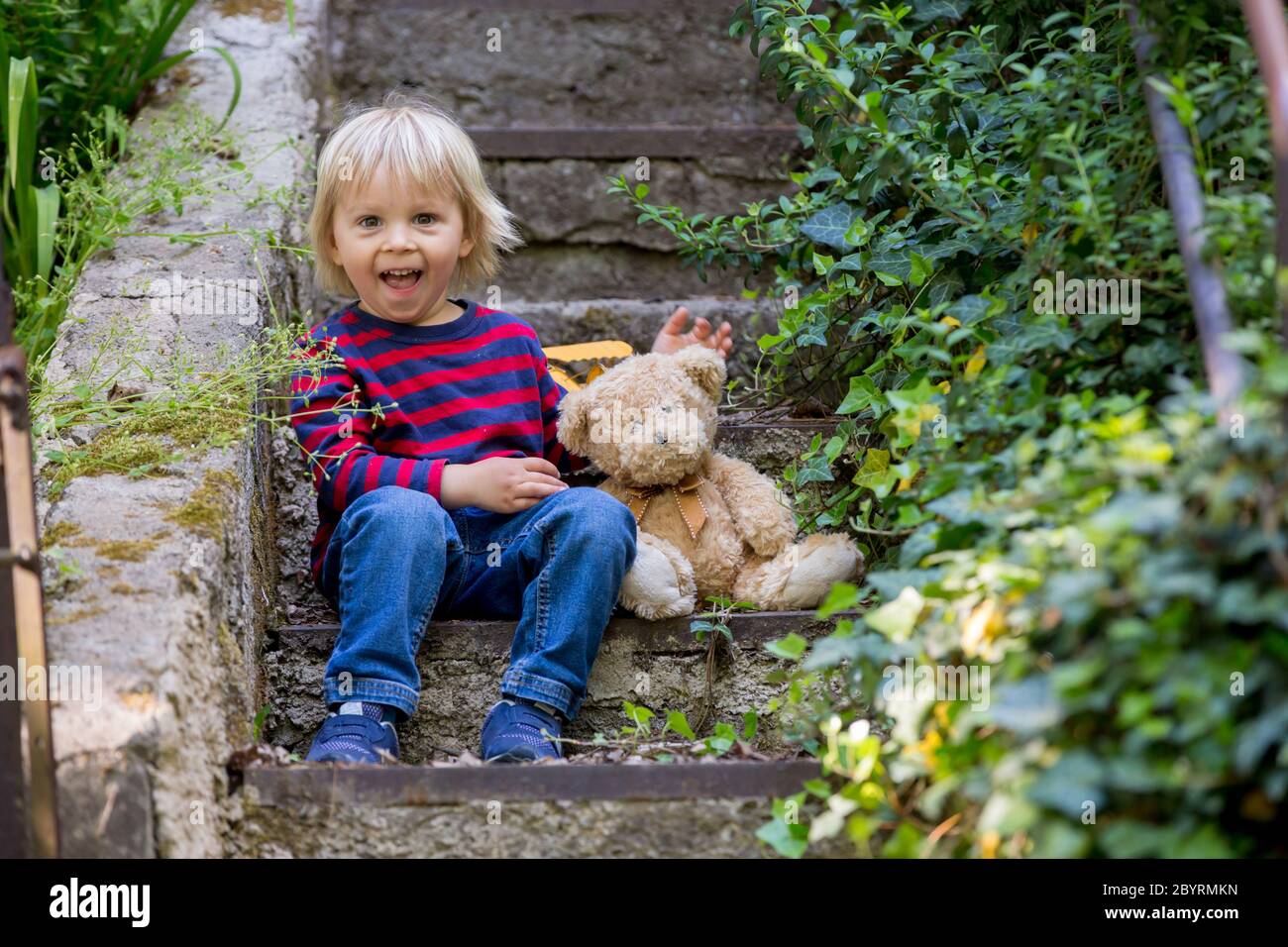 Cute little todller boy, sitting on stairs with teddy bear, playing ...